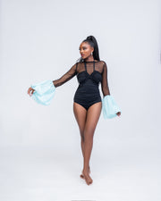 Woman wearing a black swimsuit with sheer mesh sleeves against a white background